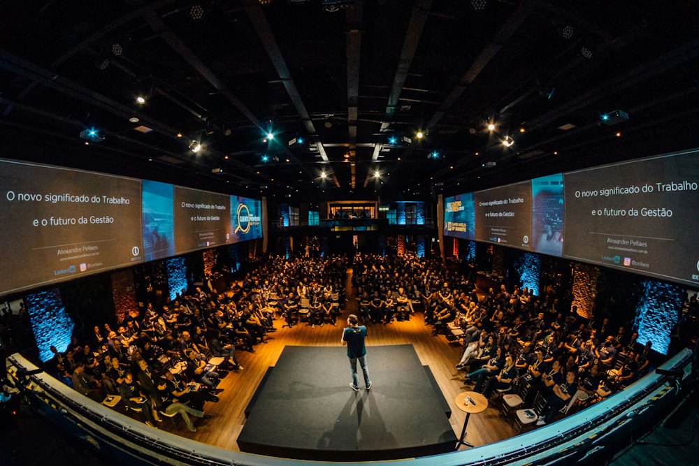A speaker on a conference stage in front of a large audience